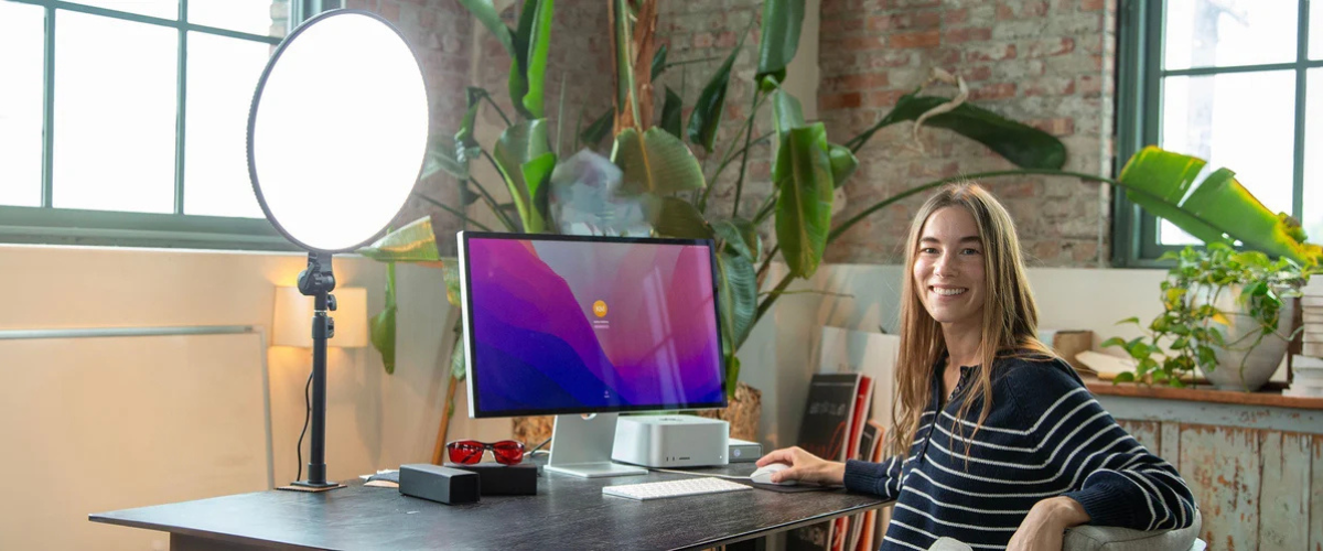 Woman in an office setting smiling at the camera next to a computer and a Chroma Sky Portal light therapy device in bright white