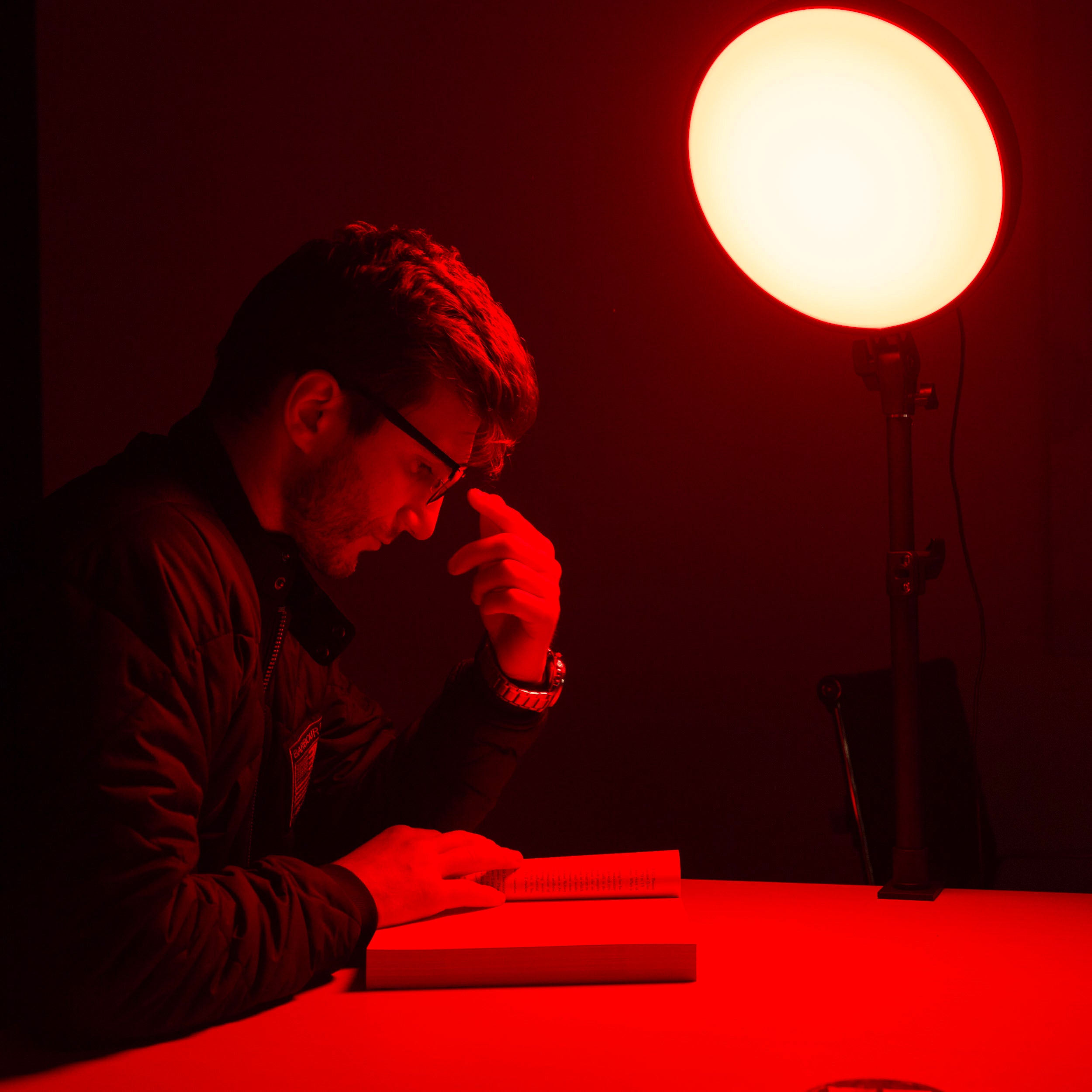 Person reading a book under a red light from a Chroma Red Portal light device on a dark background