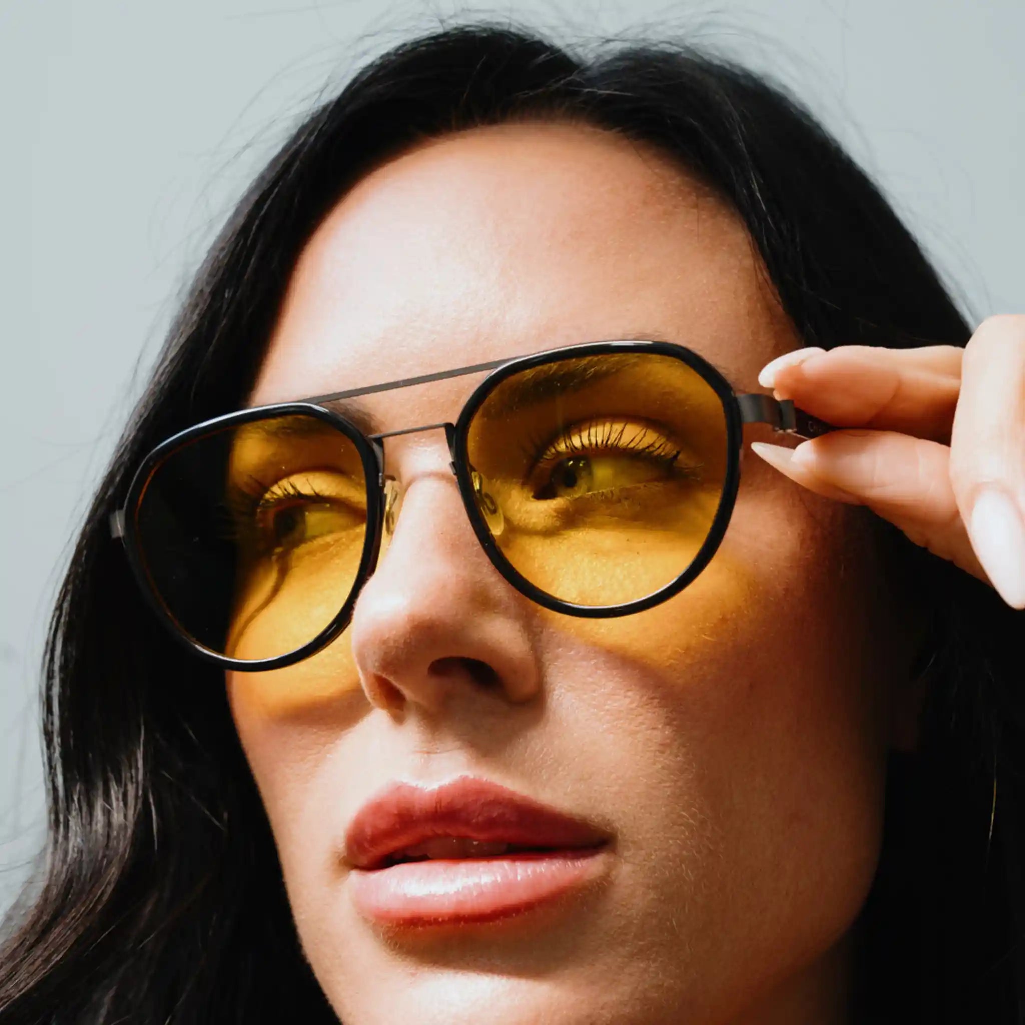 Close-up of a woman wearing Chroma Golden Glo yellow tinted glasses against a neutral background