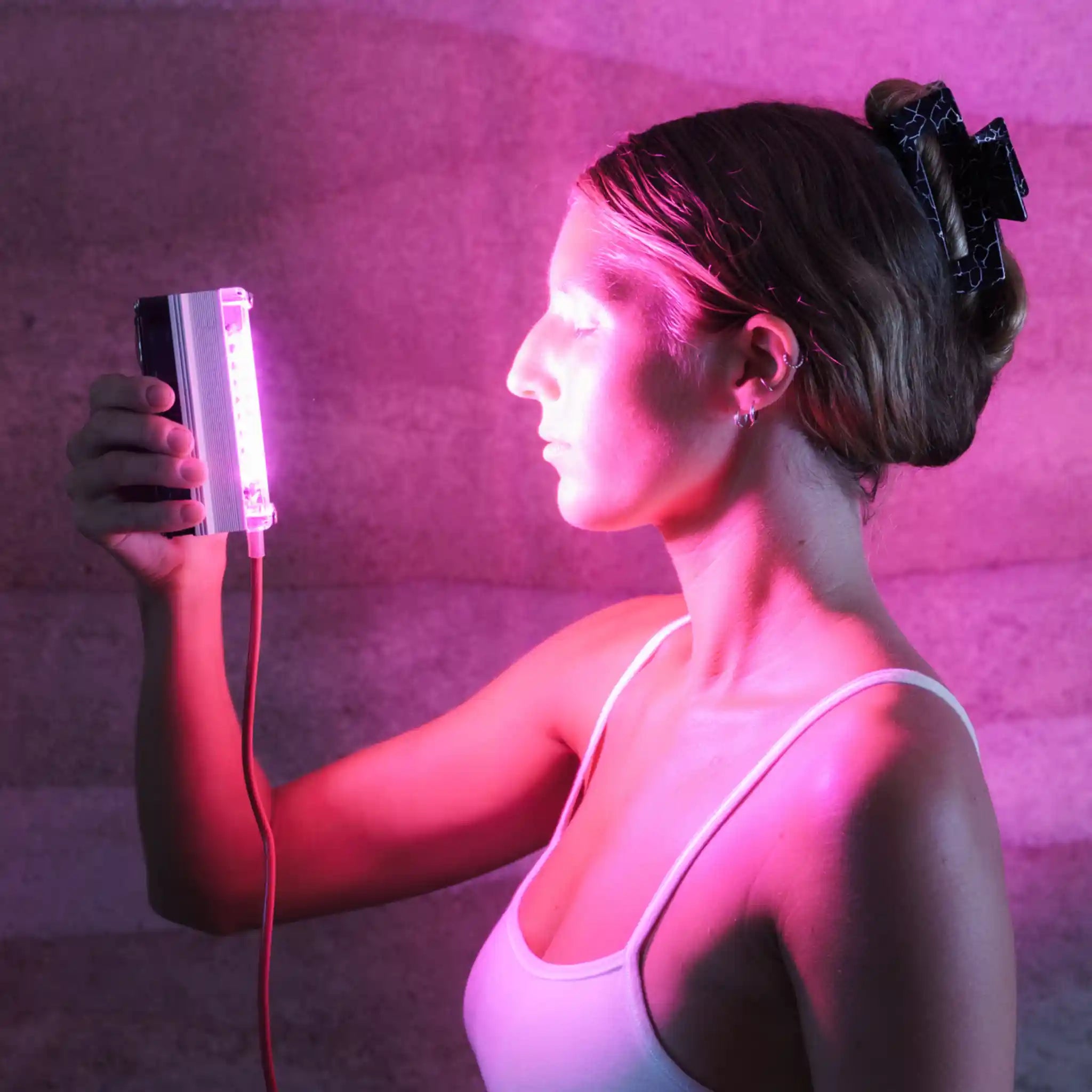 Woman holding a Chroma Radiance light therapy device emitting pink light against a dark grey and pink background