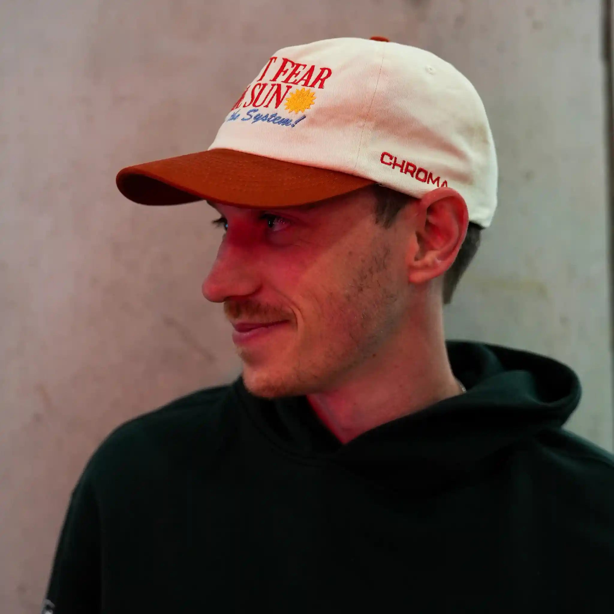 Man wearing a white cap and red cap with Chroma branding on the side against a neutral background