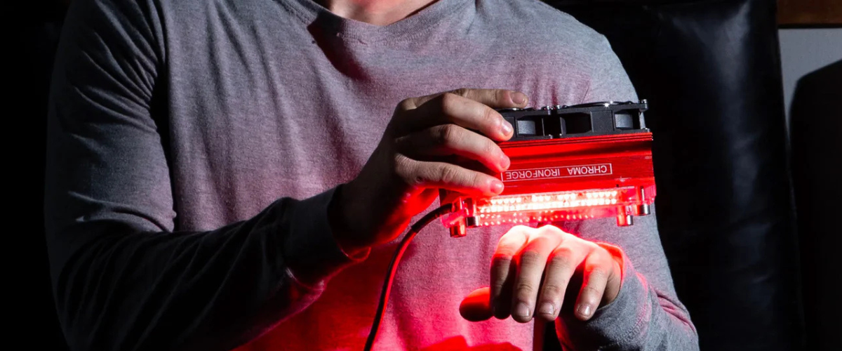 Person holding a Chroma Ironforge red & NIR light therapy device above their hand emitting a red light