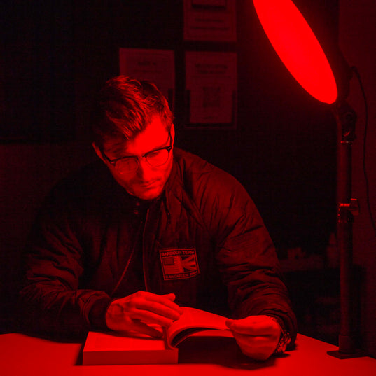 Person sitting in a dark room with red lighting from a Chroma Red Portal light device, reading a book.