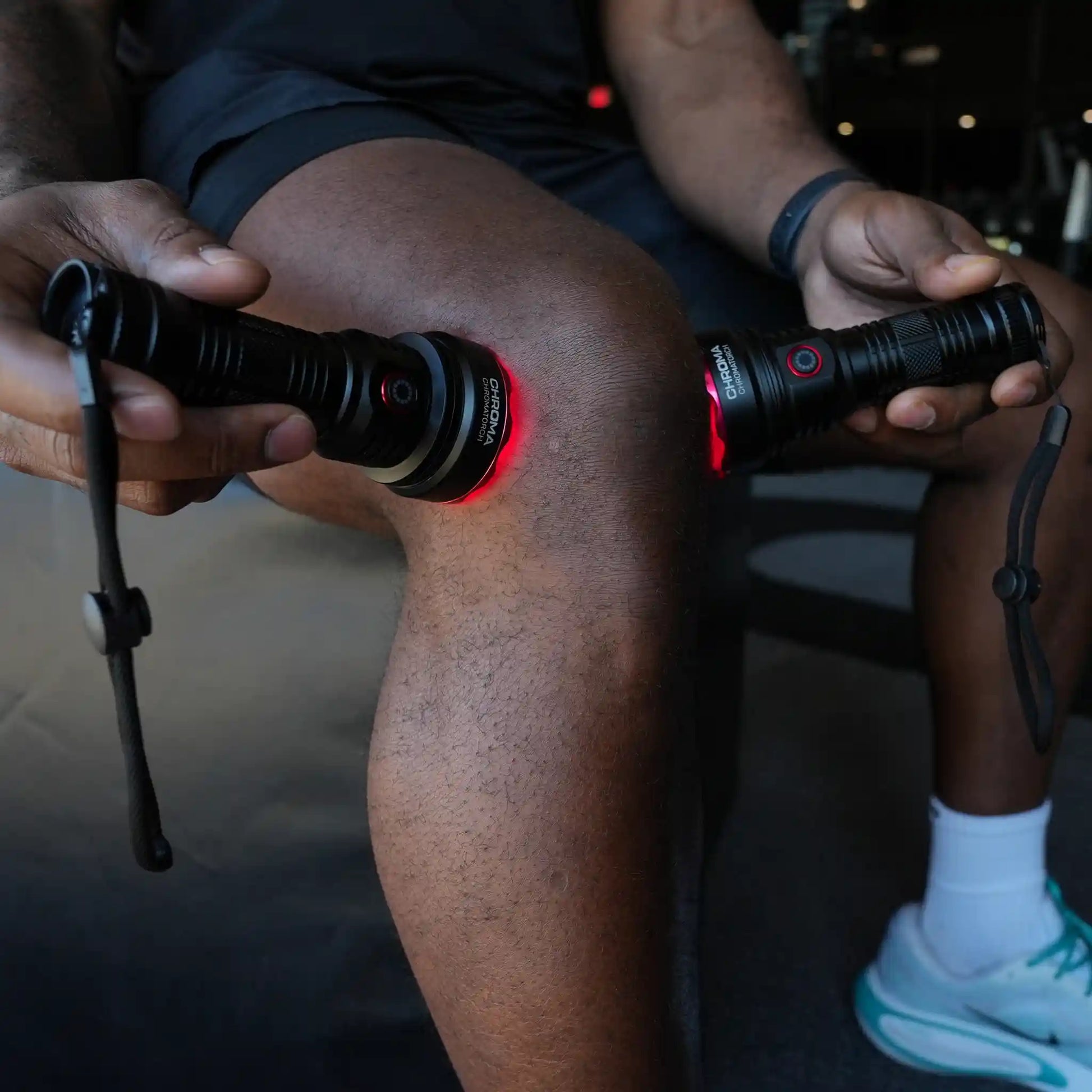 Person holding two torches (Chromatorch) against their knee with red lights on a dark background