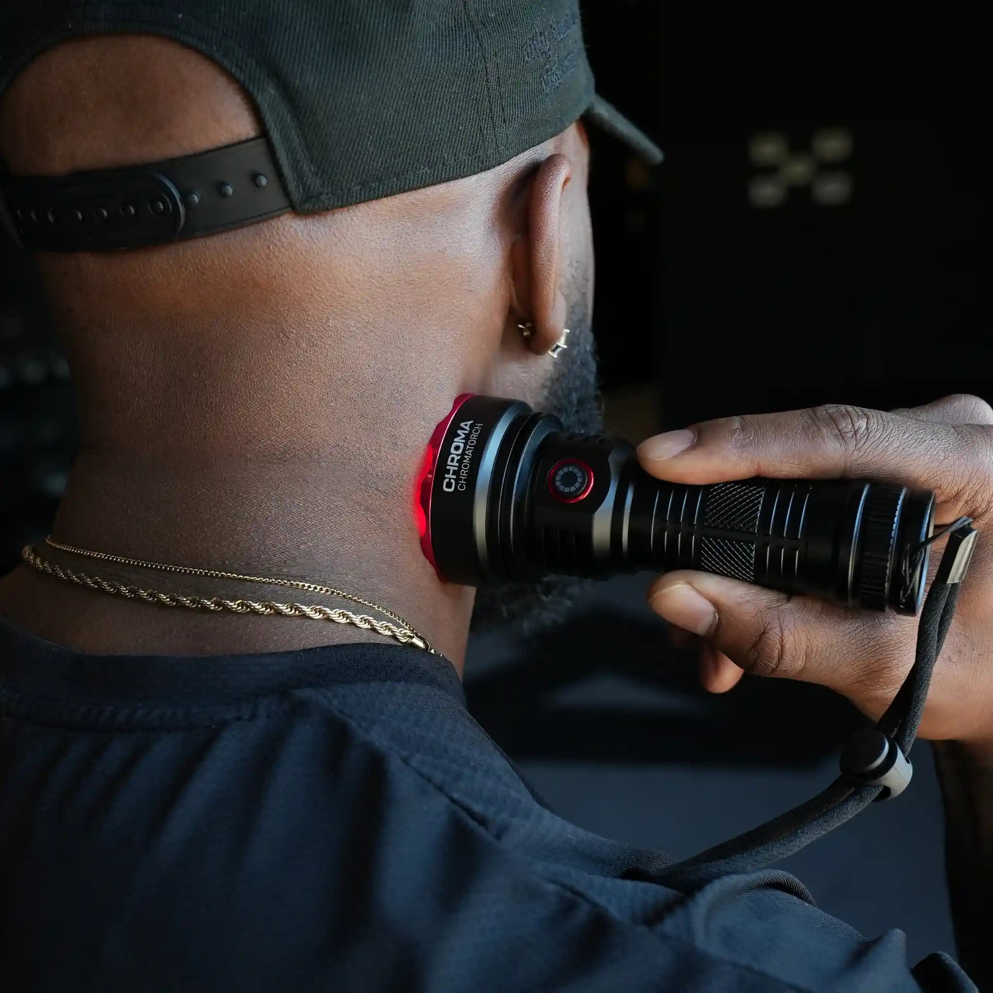 Person holding a torch (Chromatorch) with a Chroma brand logo, wearing a cap and dark clothing pressing the torch against their neck.