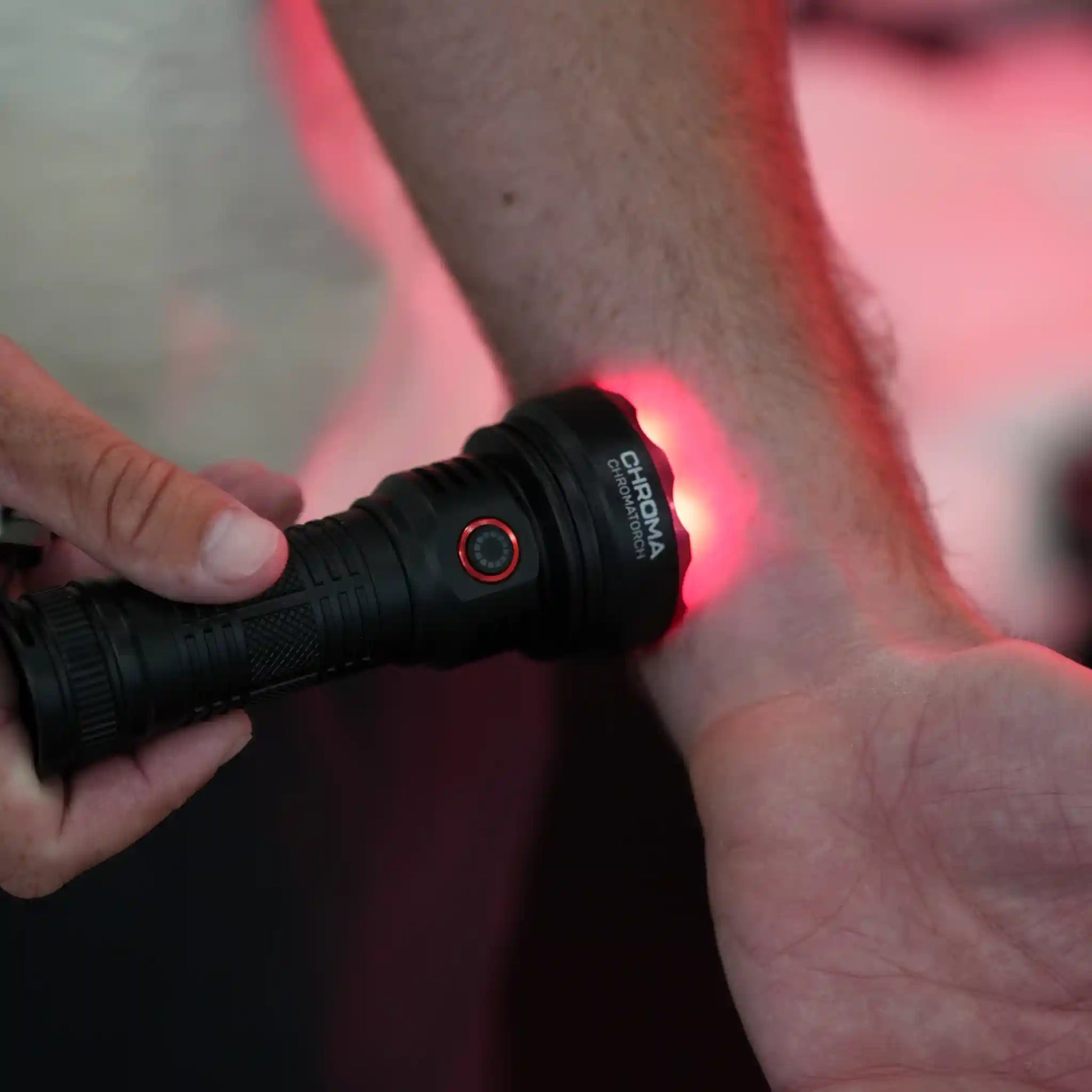 Person using a black flashlight (Chromatorch) with a red light on a blurred background