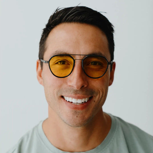 Man wearing yellow-tinted sunglasses (chroma golden glos) smiling against a plain background