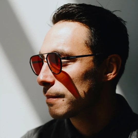 Man wearing red tinted glasses (Chroma nightshades) looking off to the side with a light rays on face against a plain background