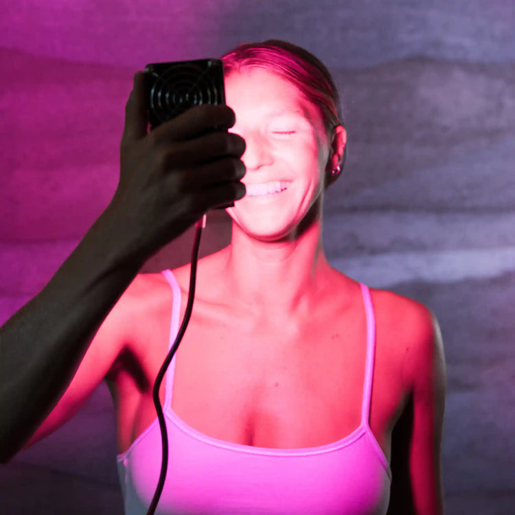 Woman holding a Chroma Radiance light therapy device in front of her face smiling against a pink and grey background