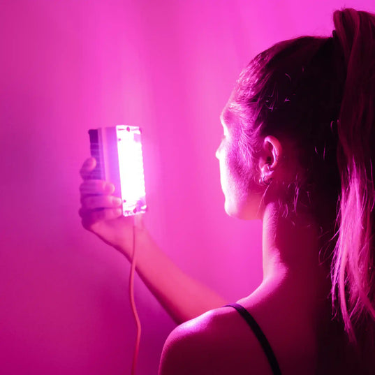 Woman holding a Chroma Radiance light therapy device emitting a pink light facing away from the camera 