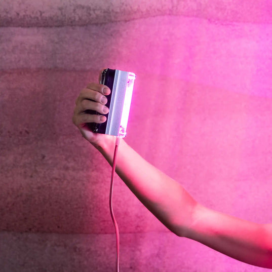 Hand holding a Chroma Radiance light therapy device emitting a red light against a pink and grey background