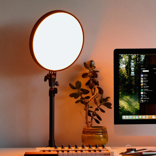 Chroma Sky Portal light device on a stand next to a computer monitor and plant on a desk.