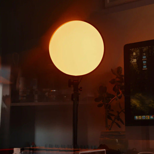 Round Chroma Sky Portal light device emitting a warm glow in a dimly lit room with a computer monitor and plant.