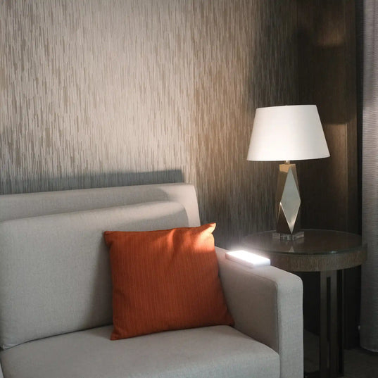 Chroma Sky Portal Mini on the armrest of a gray sofa with an orange pillow and a lamp on a side table against a textured wall.