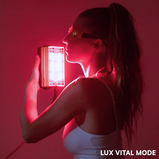 woman using a Chroma trinity red light therapy device with text 'LUX VITAL MODE' against a red background